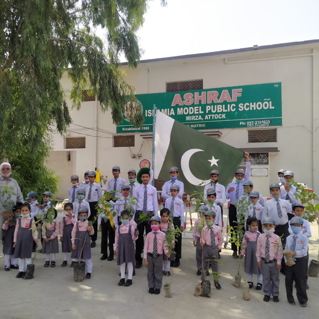 Students and teachers holding saplings and national flag in front of Ashraf Islamia Model Public School Mirza, Attock building